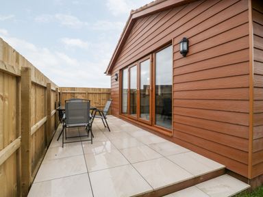 An outdoor patio with tiled floor a table and chairs next to a wooden cabin and fenced yard at Bluebell Lodge Meadow view lodges in Brean