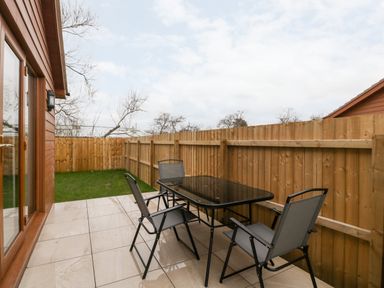 A patio area with a glass table and four chairs next to a wooden fence at Bluebell Lodge Meadow view lodges Brean