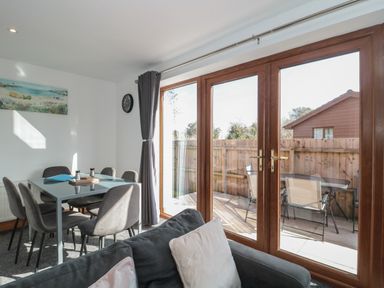 A dining area with a table and six chairs next to large glass doors leading to an outdoor patio at Bluebell Lodge Meadow view lodges in Brean