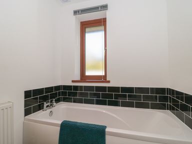 A bathroom with a bathtub below a window and black tiled walls at Bluebell Lodge Meadow view lodges in Brean