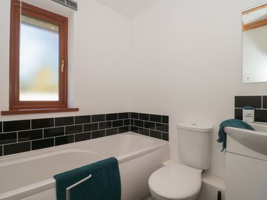 A bathroom with a bathtub a toilet and a sink with a mirror and teal towels at Bluebell Lodge Meadow view lodges in Brean