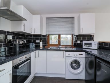 A kitchen with white cabinets black countertops appliances and a window with blinds at Bluebell Lodge Meadow view lodges in Brean