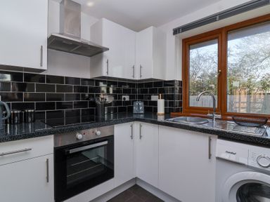 A kitchen with black tiled backsplash white cabinets a stainless steel oven and stove a sink under a window and a washing machine at Bluebell Lodge Meadow view lodges Brean