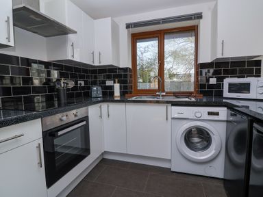 A kitchen with white cabinets black tiled backsplash appliances and a window at Bluebell Lodge Meadow view lodges in Brean
