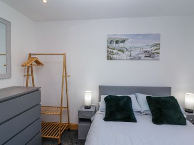 A bedroom with a bed, bedside tables with lamps, a chest of drawers, a clothes rack with hangers, and a beach-themed painting on the wall at Bluebell Lodge Meadow view lodges in Brean