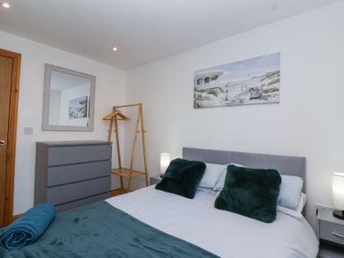 A bedroom with a bed two pillows a blanket a dresser a standing rack a mirror and a beach painting at Bluebell Lodge Meadow view lodges in Brean