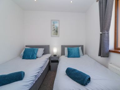 A bedroom with two single beds a nightstand and a window with curtains at Bluebell Lodge Meadow view lodges in Brean