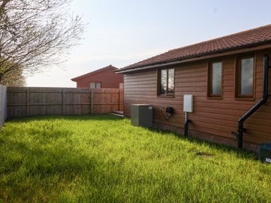 A fenced backyard with green grass and a wooden shed beside a brown house at Bluebell Lodge Meadow view lodges in Brean