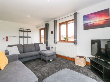 A living room with grey sofas a television on a stand and windows with grey curtains at Delphine Lodge Meadow View Lodges in Brean