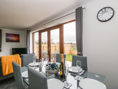 A dining room with a glass table set for six and glass doors leading to a fenced garden at Delphine Lodge Meadow View Lodges in Brean