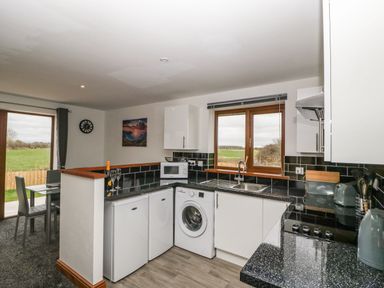 A kitchen with white cabinets two small refrigerators a washing machine microwave and a dining area with a table and chairs at Delphine Lodge Meadow View Lodges in Brean