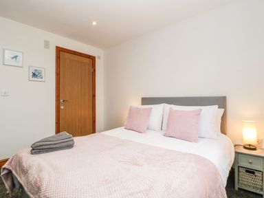 A bedroom with a bed with pink pillows and blanket a wooden door two framed pictures and a bedside table with a lamp at Delphine Lodge Meadow View Lodges in Brean