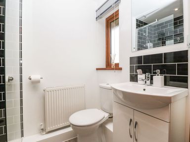 A bathroom with a toilet sink cabinet mirror and window with black tiled wall at Delphine Lodge Meadow View Lodges in Brean
