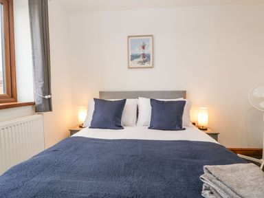 A bedroom with a bed with blue pillows and blanket bedside tables with lamps and folded towels at Delphine Lodge Meadow View Lodges in Brean