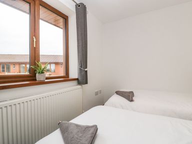 A bedroom with two single beds with towels on each and a window with a gray curtain and a plant on the windowsill at Delphine Lodge Meadow View Lodges in Brean