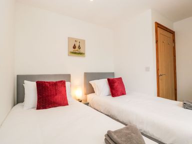 A bedroom with two single beds with red pillows and white bedding with a nightstand and lamp between at Delphine Lodge Meadow View Lodges in Brean