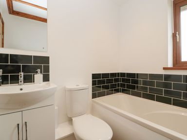 A bathroom with a white sink and cabinet a white toilet a bathtub with black tiled walls and a window at Delphine Lodge Meadow View Lodges Brean