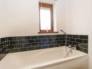 A bathroom with a white bathtub black tiled wall and a small window at Delphine Lodge Meadow View Lodges in Brean