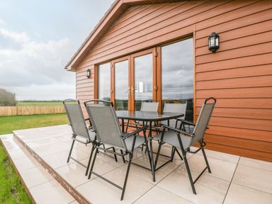 A patio with glass table and six chairs outside a building with wooden siding at Delphine Lodge Meadow View Lodges Brean