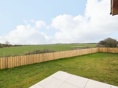 A grassy backyard with a wooden fence and open fields beyond at Delphine Lodge Meadow View Lodges Brean