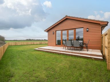 A wooden lodge with a small patio and outdoor table and chairs in a fenced grassy yard at Delphine Lodge Meadow View Lodges in Brean
