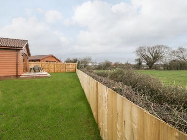 A backyard with green grass and a wooden fence around a wooden house at Delphine Lodge Meadow View Lodges in Brean