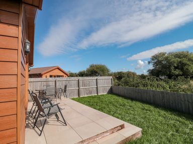 An outdoor patio area with chairs and a garden at Delphine Lodge, Meadow View Lodges Brean