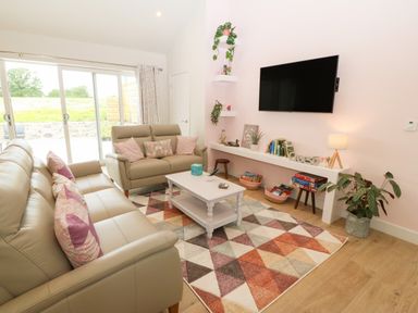 A living room with beige sofas a white coffee table a colorful triangular patterned rug and a wall mounted TV at Y Beudy in Dinas near Bontnewydd