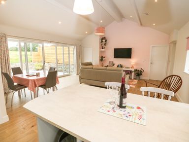An open living and dining area with a table and chairs near sliding glass doors and a sofa facing a wall mounted TV at Y Beudy in Dinas near Bontnewydd