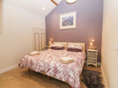A bedroom with double bed floral bedspread bedside tables lamps and a purple accent wall at Y Beudy in Dinas near Bontnewydd