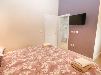 A bedroom with a bed with floral bedding a television mounted on the wall and an open door to a bathroom at Y Beudy Dinas near Bontnewydd