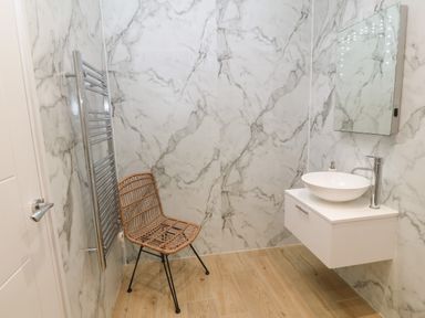 A bathroom with marble walls a wooden floor a wicker chair a wall-mounted white sink and a rectangular mirror at Y Beudy in Dinas near Bontnewydd