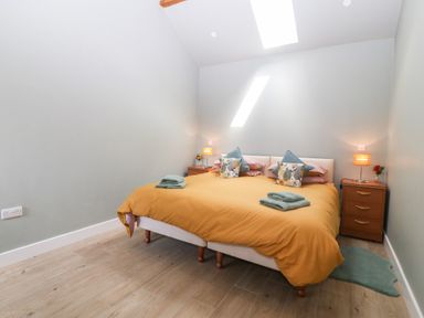 A bedroom with a large bed covered with a yellow duvet two wooden bedside tables with lamps and flowers and a skylight at Y Beudy Dinas near Bontnewydd
