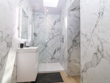 A bathroom with a white sink vanity black cup and a glass enclosed shower at Y Beudy in Dinas near Bontnewydd