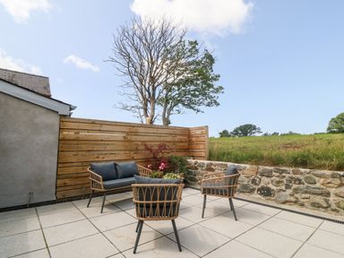 An outdoor patio with chairs and a small table with plants surrounded by a wooden fence and stone wall at Y Beudy in Dinas near Bontnewydd