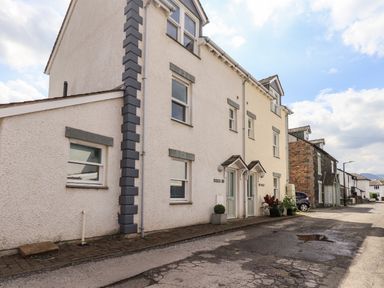 A street view of a row of white houses with multiple windows and doors with small awnings at Fell Sweep in Keswick