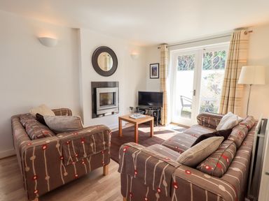 A living room with two patterned sofas a small wooden coffee table a fireplace and glass doors leading outside at Fell Sweep in Keswick