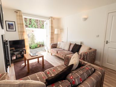 A living room with patterned sofas a wooden coffee table and a television near a patio door at Fell Sweep in Keswick