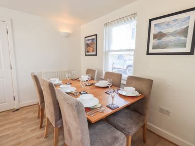 A dining room with a wooden table set for six and beige chairs at Fell Sweep in Keswick