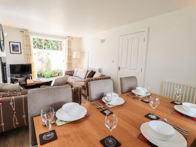 A dining table set with bowls and wine glasses next to a living room with sofas and a television at Fell Sweep in Keswick