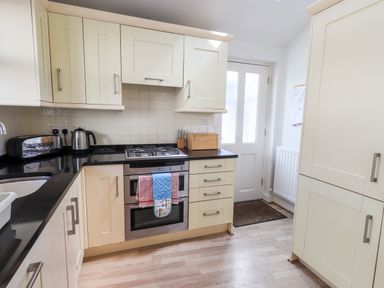 A kitchen with white cabinets a black countertop an oven a kettle a toaster and a door at Fell Sweep in Keswick