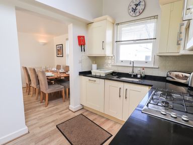A kitchen with beige cabinets a black countertop and a dining area with a wooden table and beige chairs at Fell Sweep in Keswick