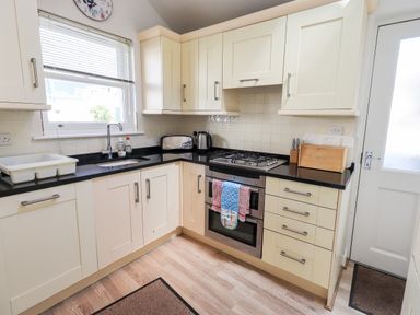 A kitchen with cream cabinets a black countertop a gas stove a sink a toaster and a bread box at Fell Sweep in Keswick