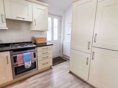 A kitchen with cream cabinets a gas stove an oven a bread box and a door at Fell Sweep in Keswick