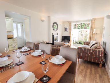 A dining table set with plates glasses and cutlery next to a living room with sofas a television and a door leading outside at Fell Sweep in Keswick