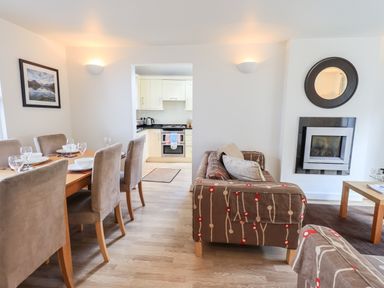 An open-plan dining and living area with a dining table and chairs on the left and a sofa facing a fireplace on the right at Fell Sweep Keswick