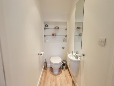 A small bathroom with a toilet sink mirror built in shelves and wooden floor at Fell Sweep in Keswick