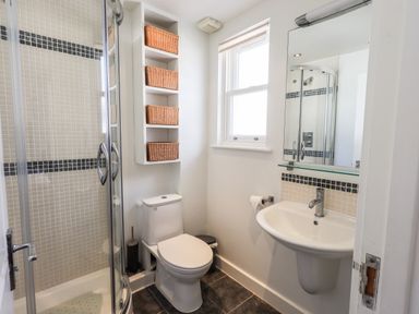 A bathroom with a shower enclosure toilet sink and wall shelves with baskets at Fell Sweep in Keswick