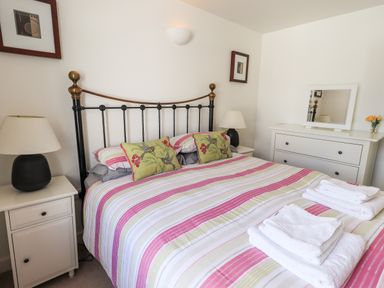 A bedroom with a striped bedspread on a metal bed frame two bedside tables with lamps a dresser with a mirror and folded towels at Fell Sweep in Keswick