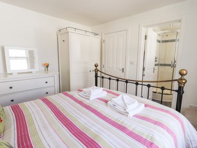 A bedroom with a striped bedspread towels on the bed a white dresser with a mirror a wardrobe and an ensuite shower at Fell Sweep in Keswick
